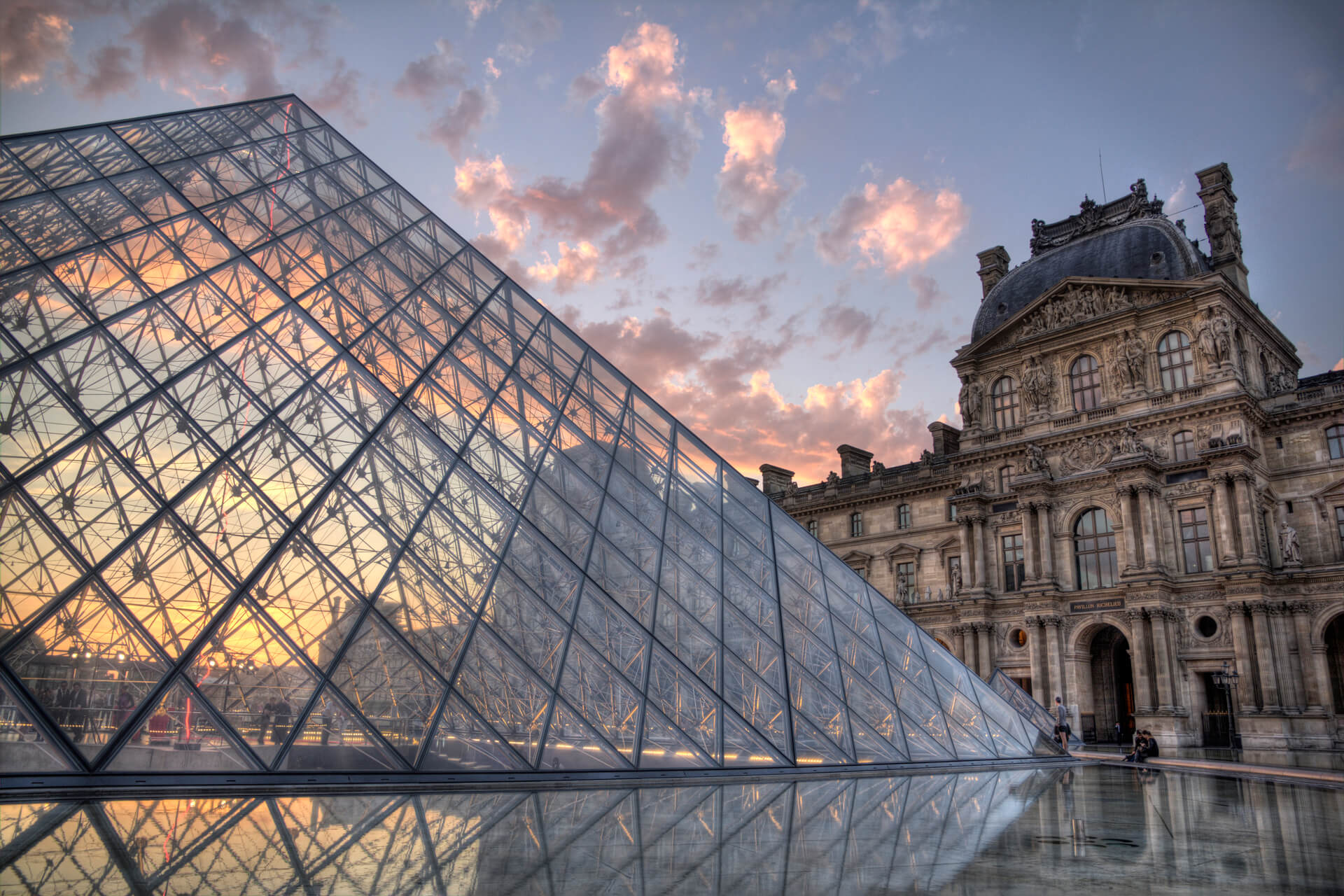 una-gran-piramide-de-vidrio-esta-al-lado-de-un-edificio-con-un-cielo-nublado-en-el-fondo (1)